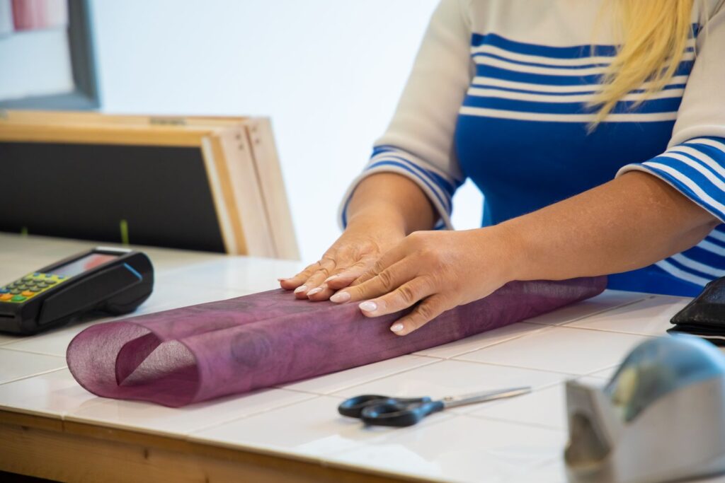 Hands wrapping a customer's gift in purple tissue paper at a shop counter