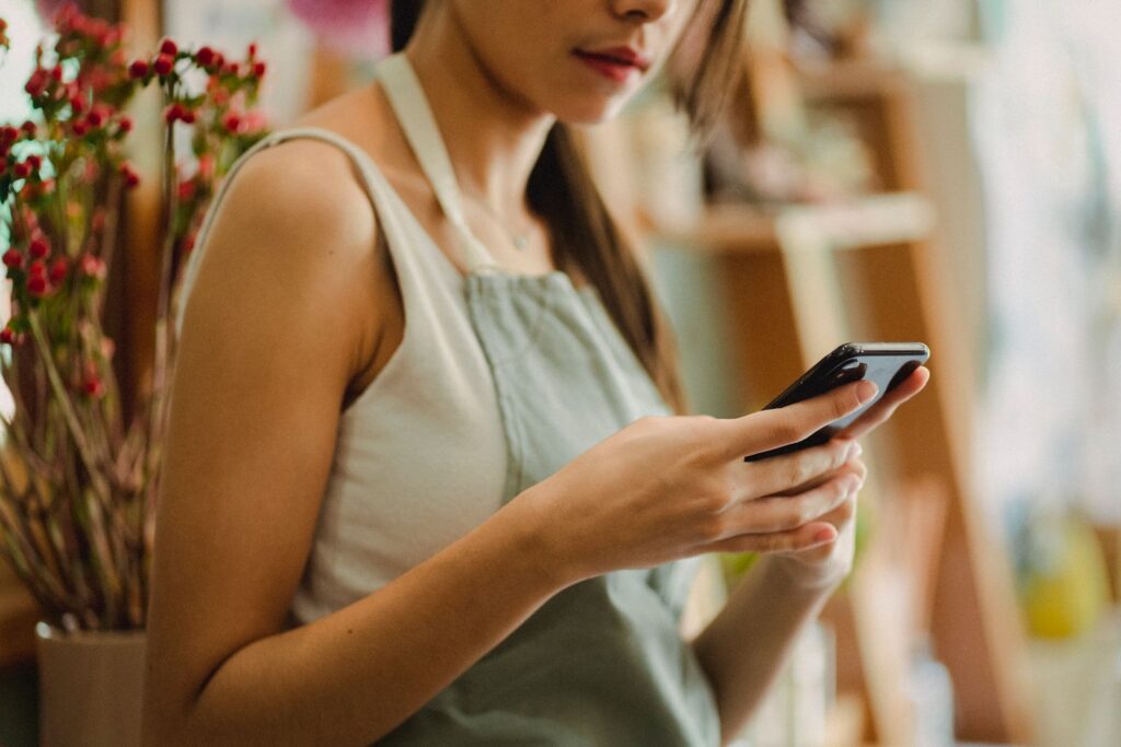 Small business owner in an apron checking her smartphone at the shop counter